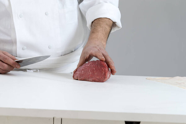 Closeup of the hands of a butcher cutting slices of raw meat off a large loin for tournedos