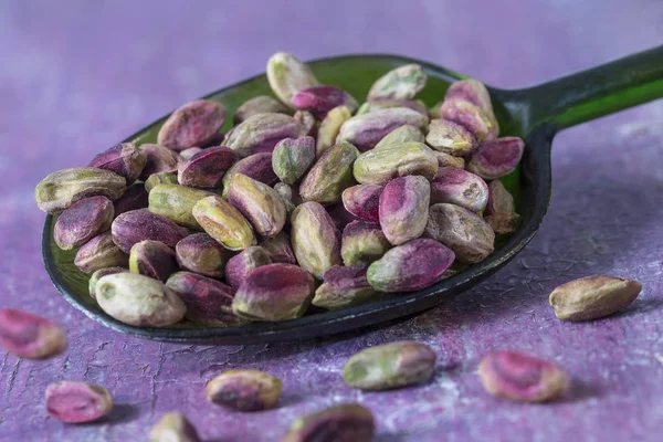 Pistachos pelados en una cuchara, aislados, fondo de madera púrpura — Foto de Stock