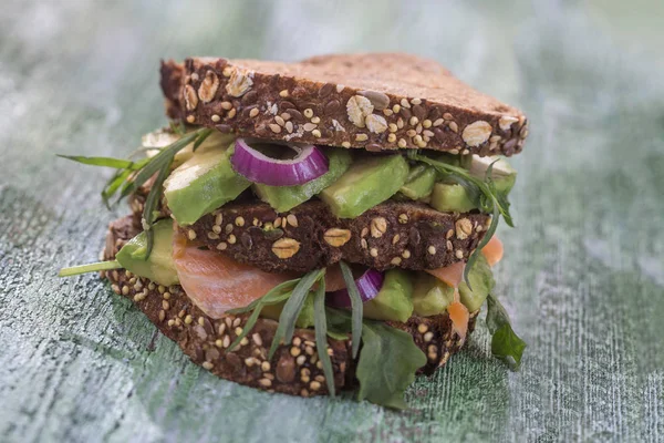 Countrybread avokado, tuzlanmış somon sandviç taze sürüler üzerinde yeşil aileninde paintt ahşap tahta arka plan ile. Sağlıklı yeme Tema