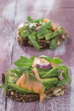 Countrybread avokado, tuzlanmış somon sandviç taze otlar üzerinde pembe aileninde paintt ahşap tahta arka plan ile. Sağlıklı yeme Tema