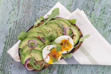 Kepekli ekmek avokado, taze otlar ile haşlanmış yumurtalı sandviç, Bulaşık bezi ahşap tahta arka plan üzerinde kırmızı soğan. Sağlıklı yeme Tema