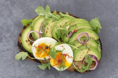 whole wheat bread Avocado, poached egg sandwich with fresh herbs ,redonion, on grey slate background clipart