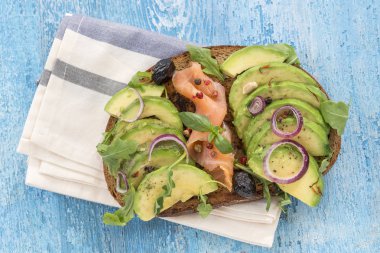 Kepekli ekmek avokado, taze otlar, kırmızı soğan Bulaşık bezi ahşap tahta arka plan ile smocked somon sandviç. Sağlıklı yeme Tema