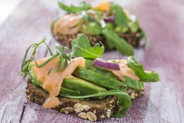 Countrybread avokado, tuzlanmış somon sandviç taze otlar üzerinde pembe aileninde paintt ahşap tahta arka plan ile. Sağlıklı yeme Tema