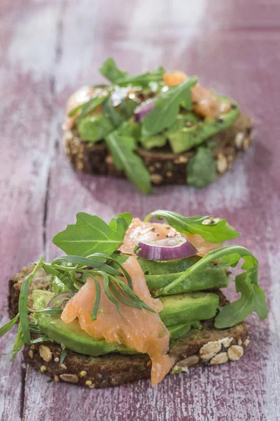 Countrybread avokado, tuzlanmış somon sandviç taze otlar üzerinde pembe aileninde paintt ahşap tahta arka plan ile. Sağlıklı yeme Tema