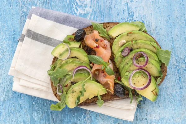Kepekli ekmek avokado, taze otlar, kırmızı soğan Bulaşık bezi ahşap tahta arka plan ile smocked somon sandviç. Sağlıklı yeme Tema