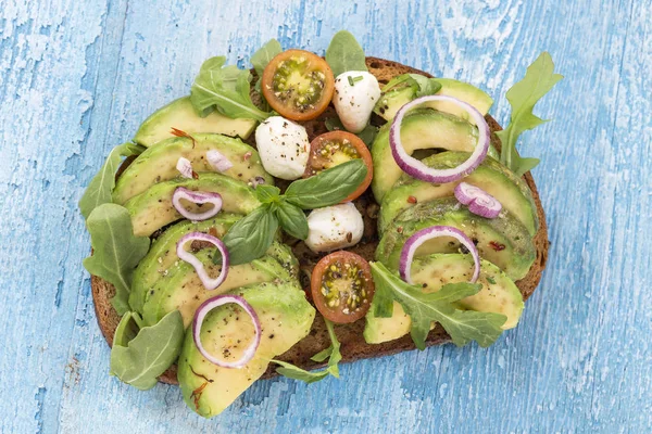 Kepekli ekmek avokado, domates, taze otlar, kırmızı soğan Bulaşık bezi ahşap tahta arka plan ile mozzarrela sandviç. Sağlıklı yeme Tema