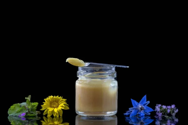 Raw organic royal jelly in a small bottle with litte spoon on black surrounded by flowers — Stock Photo, Image