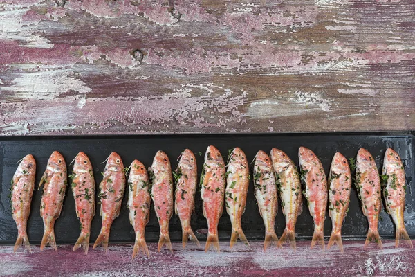 Plenty of red mullet fish ready to grill on placha barbecue on a pink wooden booard