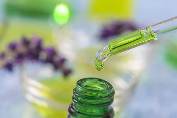 Groene glazen flessen met druppels Lavendel essentiële vloeistof in de pipet op houten achtergrond met medicinale bloemen — Stockfoto