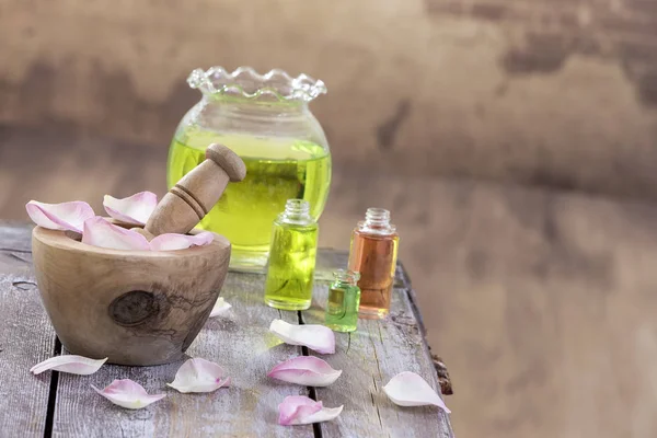 Spa- und Wellness-Konzept: Zubereitung von ätherischem Öl mit rosa Rosen, einer Flasche Tinktur und Mörtel auf einem Holzbrett mit Vintage-Wand — Stockfoto