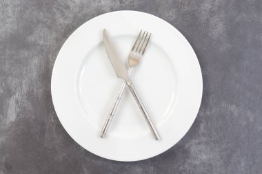 Beyaz tabak, çapraz çatal ve bıçak yukarıdan gri plastik dokulu masa yüzeyi