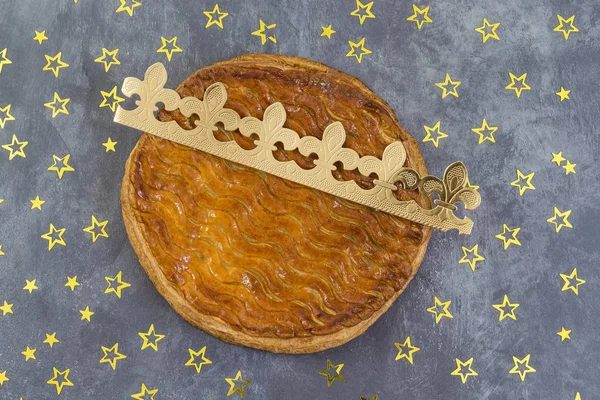 Galette des rois, gâteau royal français avec une couronne dorée sur fond d'ardoise grise parsemée d'étoiles dorées — Photo
