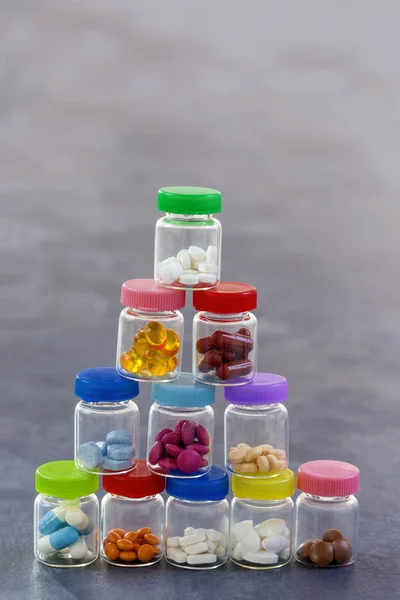 Pilha de comprimidos de medicina em caixa de vidro com tampas plásticas multi coloridas em fundo de ardósia cinza — Fotografia de Stock