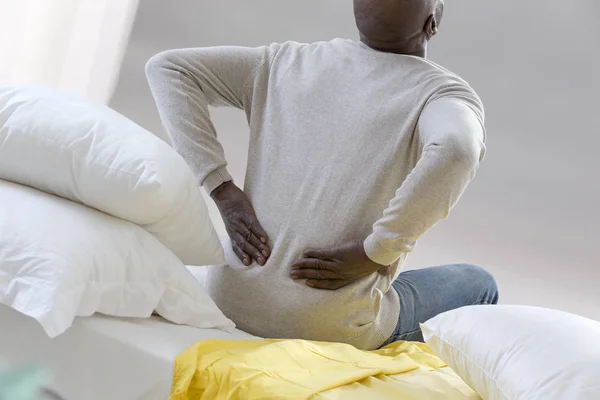 Афроамериканец с сильной болью в спине сидит на кровати в своей спальне — стоковое фото