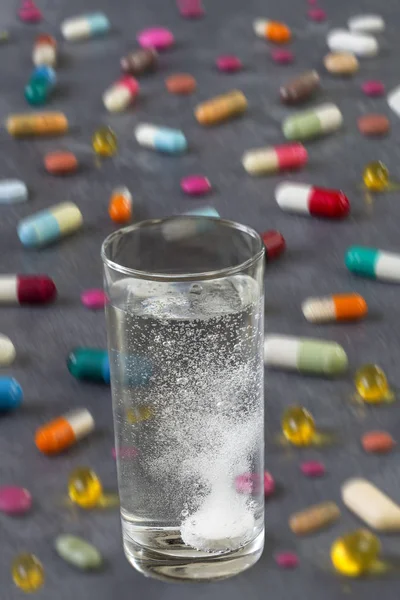 Compressa effervescente in acqua con bolle con pillole multicolori e capsule su fondo grigio ardesia — Foto Stock