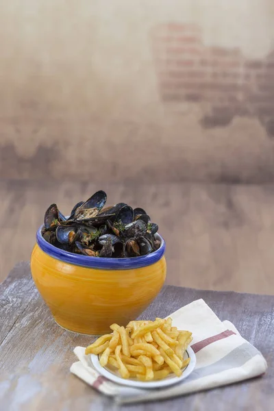 French blue mussel with herbs in a yellow bowl with french fries glass ramekin on napkin Seafood in a wooden board in vintage wall background — Stock Photo, Image