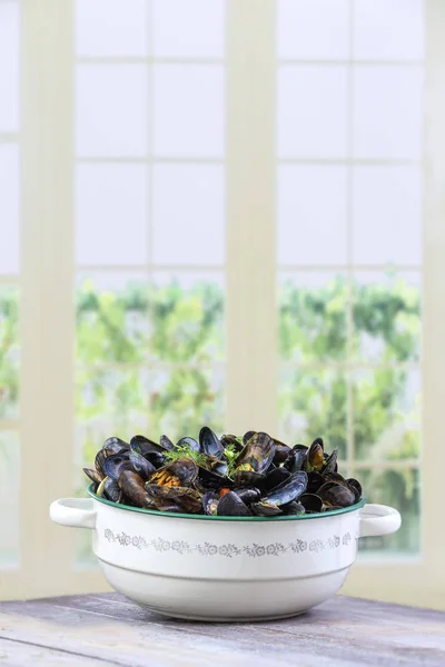 Mejillones azules franceses cocidos con perejil en una olla antigua de esmalte vintage sobre un fondo de ventanas de cocina — Foto de Stock