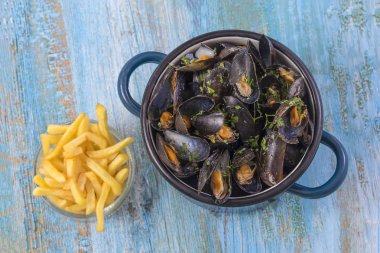 Midye mavi ahşap arka plan üzerinde mavi bir seramik tencerede. bir cam kase patates kızartması. Sıcak yaşam tarzı.