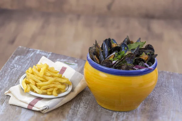 Franska blåmusslor med örter i en gul skål med pommes frites glas ramekin på servett skaldjur i en träskiva bakgrund — Stockfoto