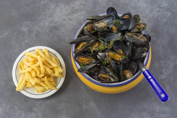 Moule bleue française aux herbes dans un bol jaune avec ramequin en verre frites sur serviette en pierre grise — Photo