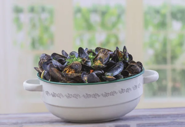 Mejillones azules franceses cocidos con perejil en una olla antigua de esmalte vintage sobre un fondo de ventanas de cocina — Foto de Stock