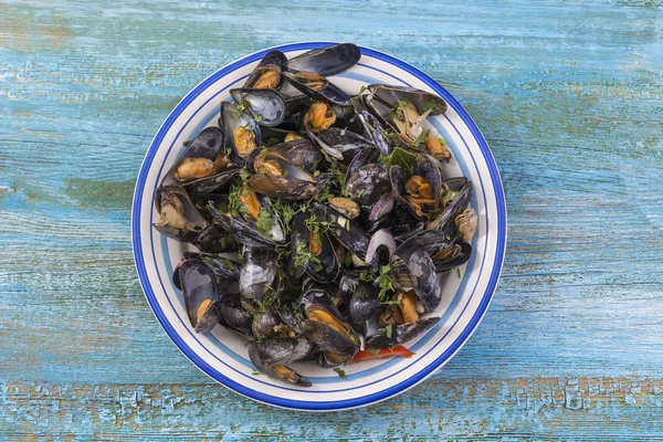 Mexilhões cozidos no vapor em vinho branco com ervas, frutos do mar. Servido em placa branca, vista para cima em fundo de madeira azul — Fotografia de Stock