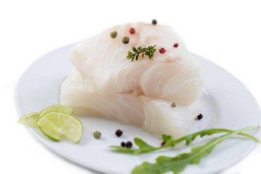 close up Fresh raw cod fish fillet on a plate with parsley and lemon isolated white background clipart