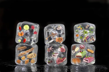 Dondurulmuş ürünler kavramı: meyve, sebze, fishs, eti, baharat otlar, pasta, siyah arka plan üzerine buz küpleri içinde donmuş