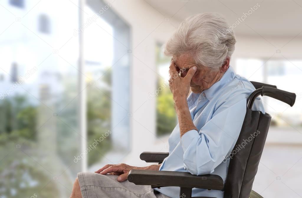 Side view of lonely old woman in wheelchair in front of a glass windows corridor