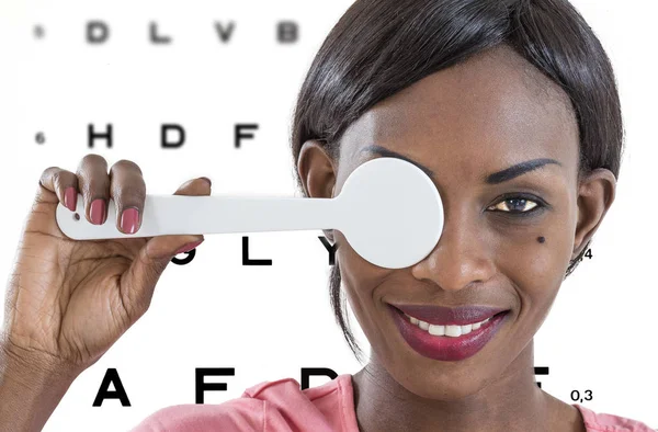 Joven mujer africana tomando un examen de la vista en una clínica óptica con ilustraciones de la carta de los ojos en el fondo — Foto de Stock