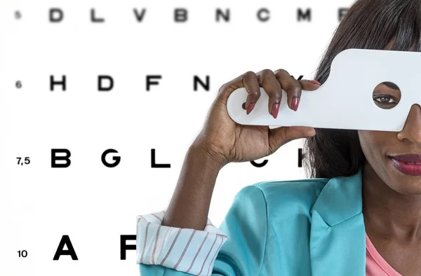 Молодая африканская женщина проходит обследование зрения в оптической клинике с иллюстрациями на заднем плане. — стоковое фото