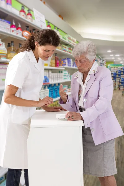 medicine, pharmaceutics, health care and people concept - happy pharmacist showing drug lnstruction to senior woman customer at drugstore