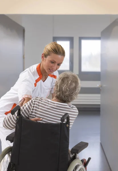 Enfermera ayudando a la señora discapacitada en levantarse en grande, ventanas, fondo, coridor — Foto de Stock