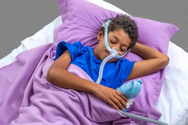 Niño que sufre de apnea del sueño, con una máscara respiratoria . — Foto de Stock