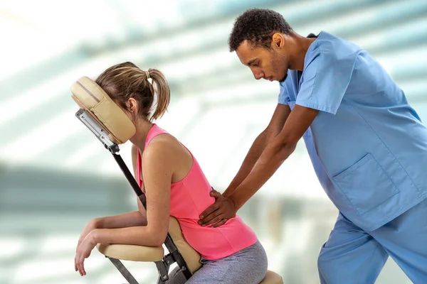 안마 의자에 앉아 있는 환자에게 마사지를 해 주는 물리 치료사 — 스톡 사진