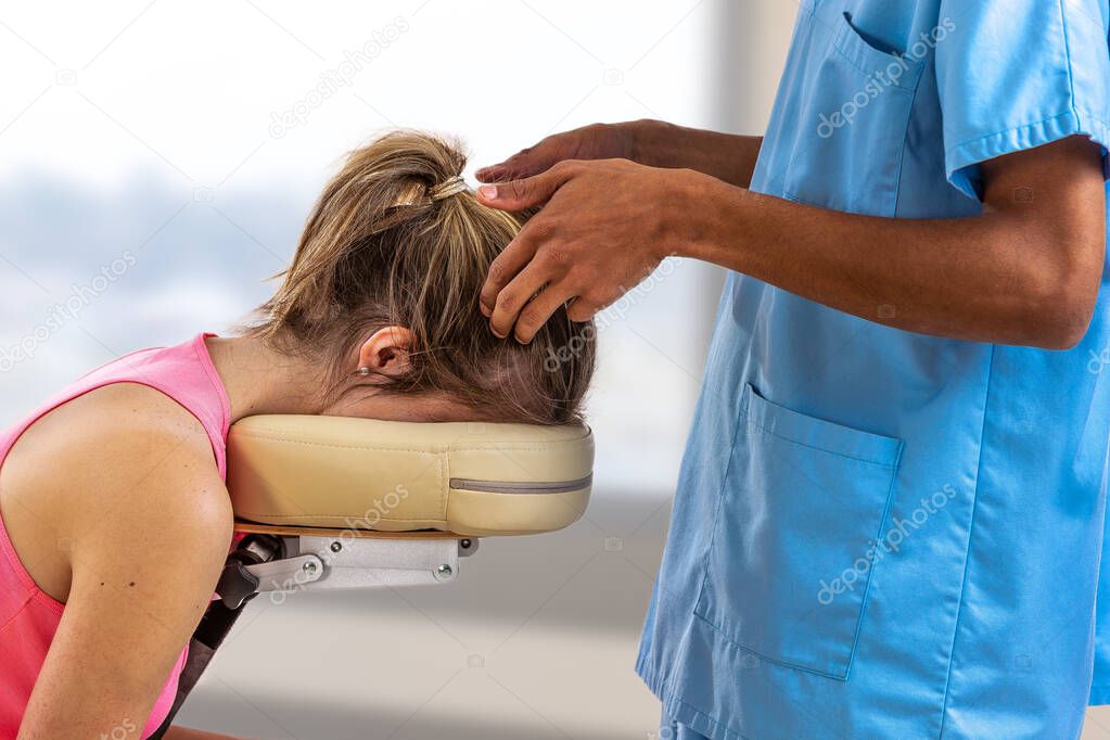 Woman lying on the back while being massaged on her head in a room by a physiotherapist on a massage chair