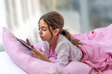 Yatakta oynayan küçük kız dijital tablet. Pembe keten üstten manzaralı
