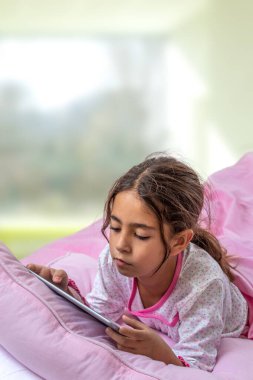 Dijital tablet kullanan küçük kızlar yatakta oynuyorlar. Pembe keten üstten manzaralı