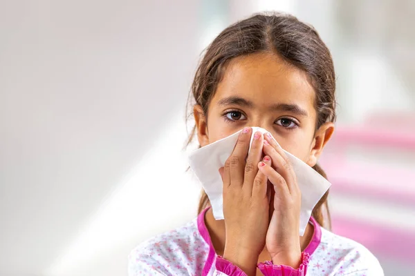 Niña linda estornudando en un pañuelo sonándose la nariz. tener gripe — Foto de Stock
