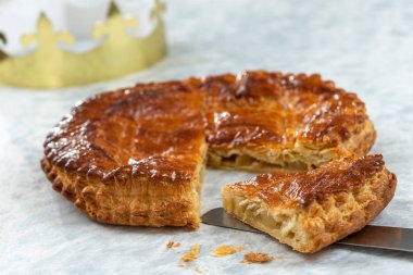 Epiphany Twelfth Night cake french galette des rois made of puff pastry, slice apart with the charm inside, open crown leaning beside