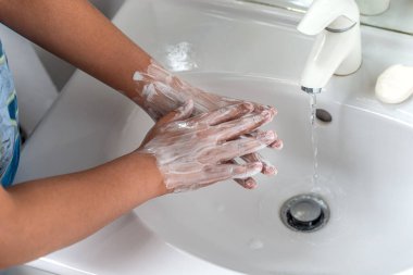 Kadın elini sabun köpüğü ve musluk suyuyla yıkıyor. Musluğun altındaki el temizliği kişisel hijyen için grip önleyici..