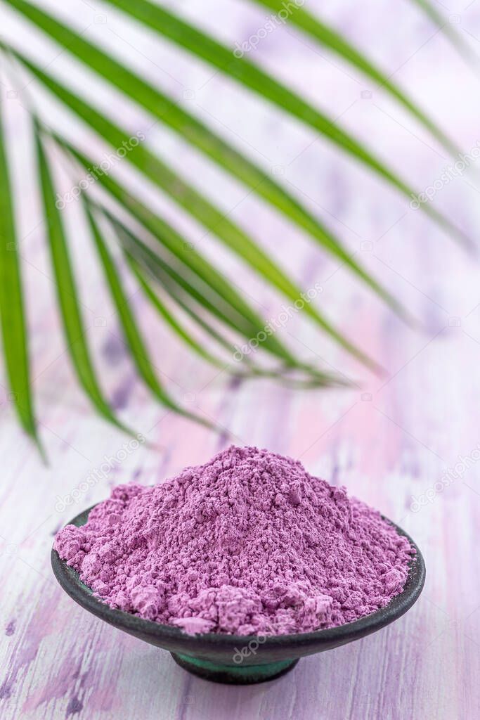 Dry pink clay powder mask for face and body in ceramic bowl isolated on purple