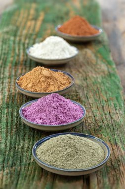 Deniz kil tozunun seramik kaseleri: kırmızı, pembe, yeşil, mor, yüz ve vücut tedavisi kavramı yeşil ahşap tahta,