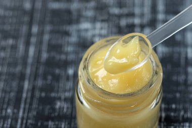 Çiğ organik kraliyet jölesi küçük bir şişede küçük bir kaşıkla siyah bir arka planda.,