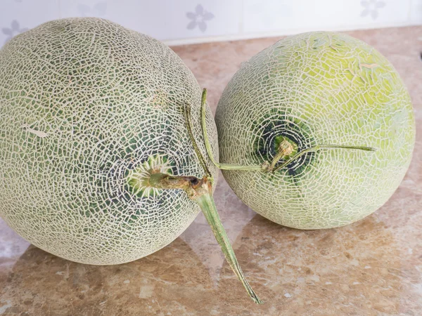 Two green japanese melons on counter in kitchen