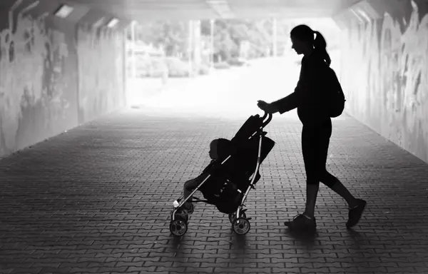 Mãe solteira andando no túnel da cidade com bebê no carrinho . Fotos De Bancos De Imagens Sem Royalties