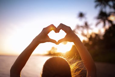 Gün batımında plajda kalp şeklinde el yapan bir kadın. Aşk ve doğa güzellik kavramı. 