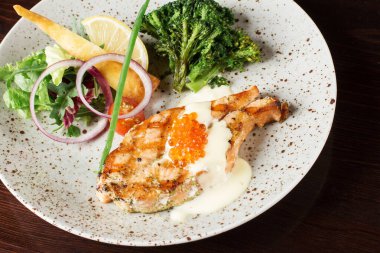 Beyaz tabakta sebzeli somon bifteği.