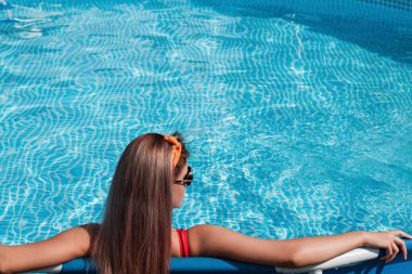 Şık bikinili seksi bir kızın moda fotoğrafı. Yüzme havuzunda güneşleniyor.